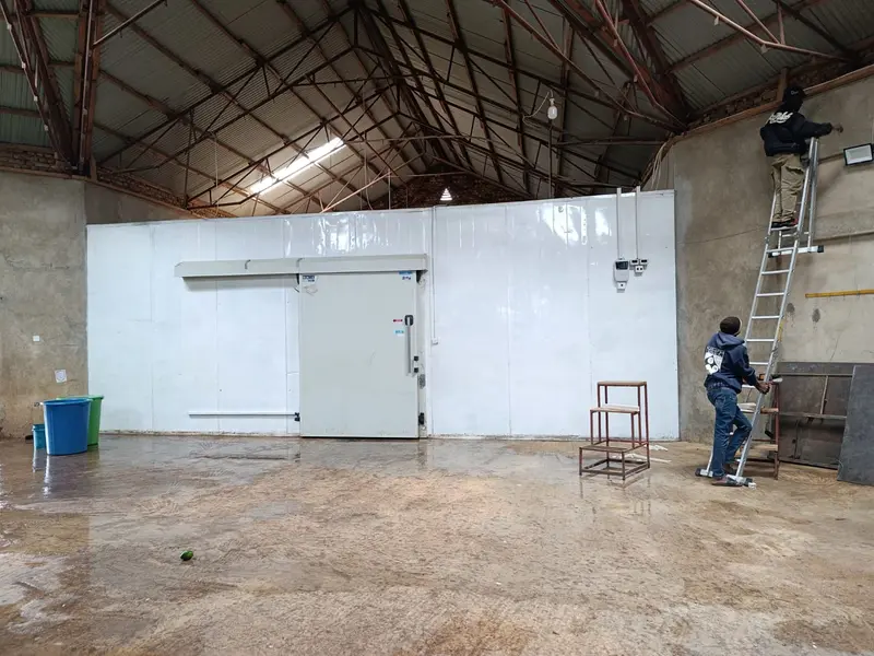 Technicians installing a white insulated-panel coldroom in a warehouse