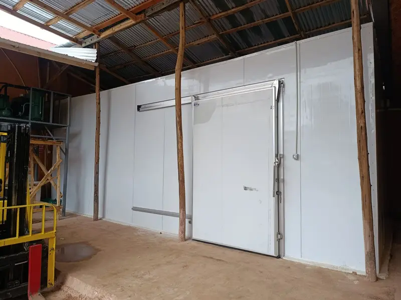 White walk-in coldroom with sliding door under a warehouse roof, with a forklift nearby